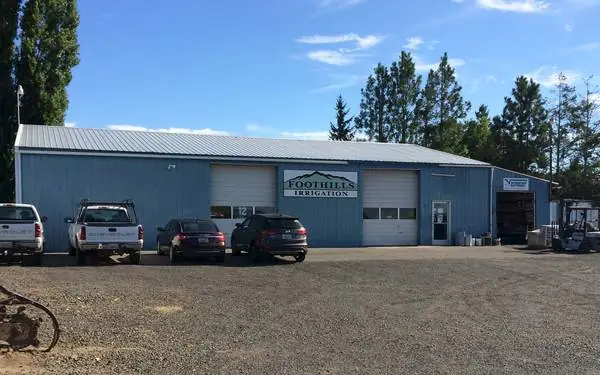 The blue steel Foothills Irrigation building with pickups in the gravel lot and a forklift by the side yard
