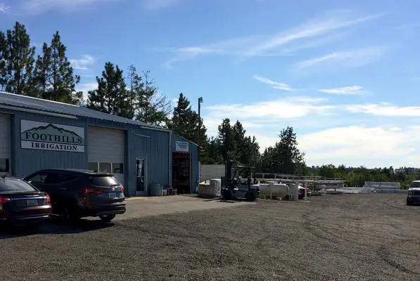 The Foothills Irrigation building from the lot, with a forklift and stacked pipe in the side yard